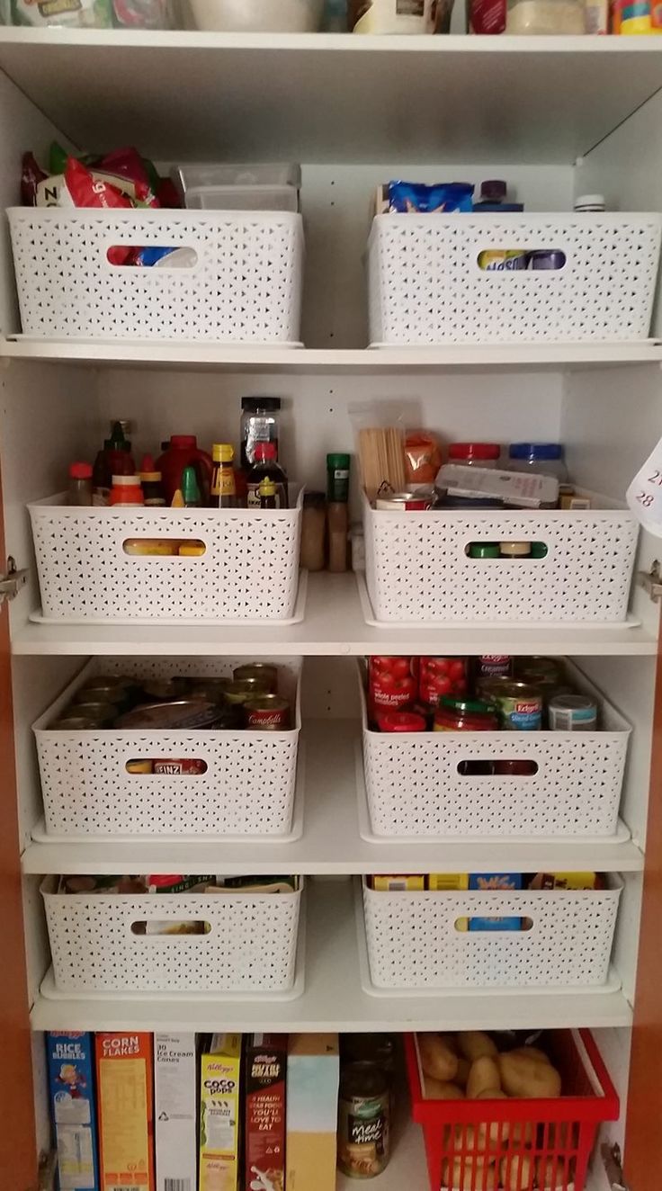 an organized pantry with white bins and plastic baskets on the bottom shelf, full of food