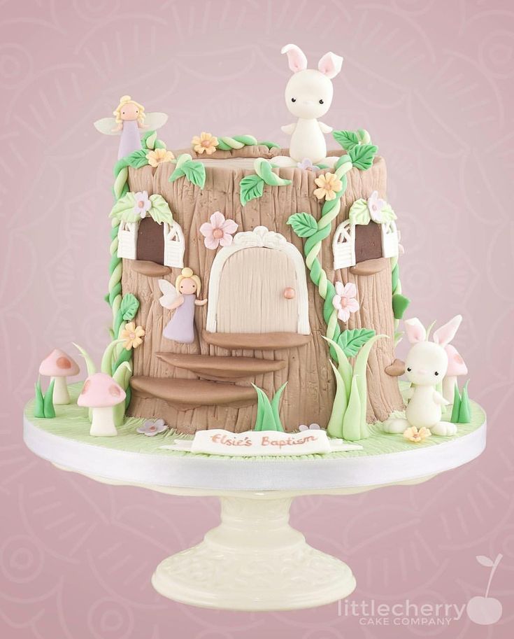 there is a cake that looks like a fairy house with rabbits on the roof and flowers around it