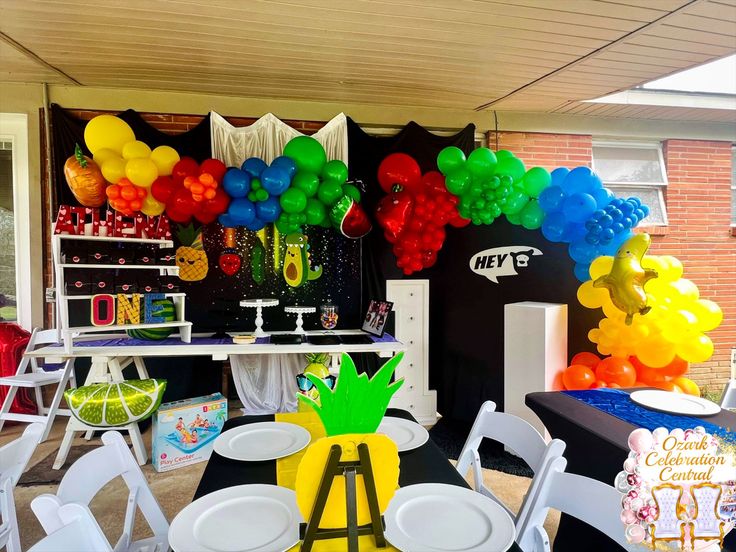 an outdoor party with balloons, pineapples and other decorations on the tables in front of it