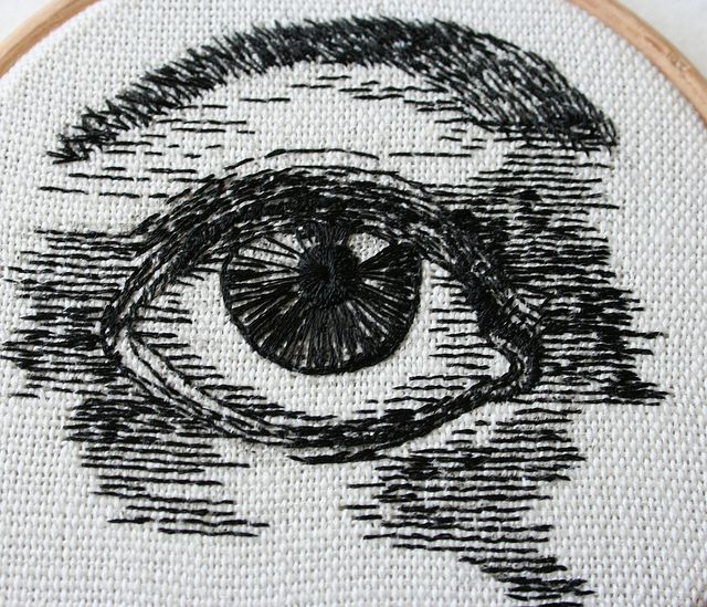 an eye is drawn in black and white on a piece of paper with thread work