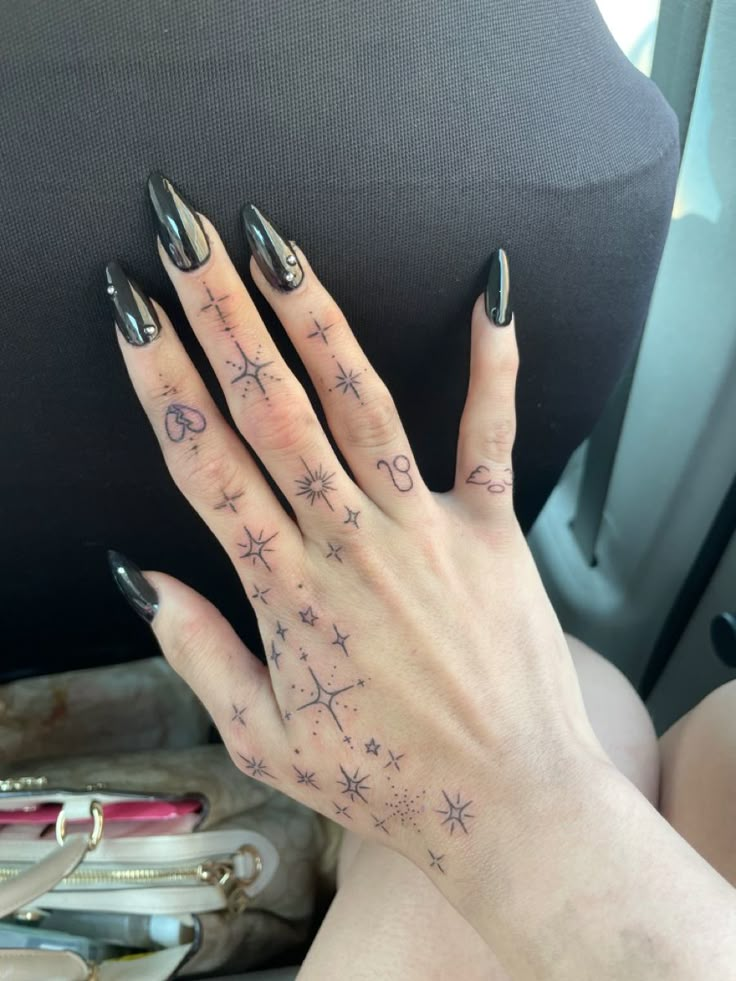 a woman's hand with stars and moon tattoos on her left hand, sitting in the back seat of a car