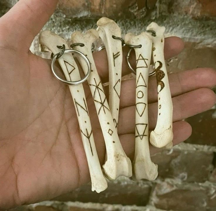 three bone keychains with symbols on them are held in someone's hand