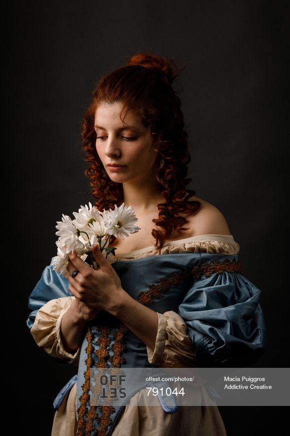 a woman with red hair holding flowers in her hand and looking down at the ground