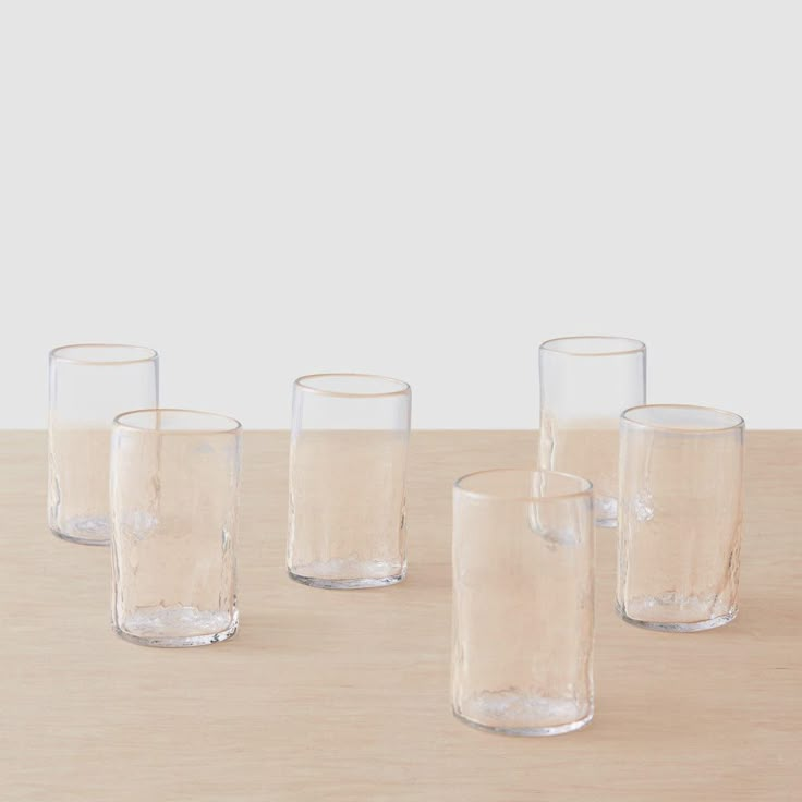 four clear glass vases sitting on top of a wooden table next to each other