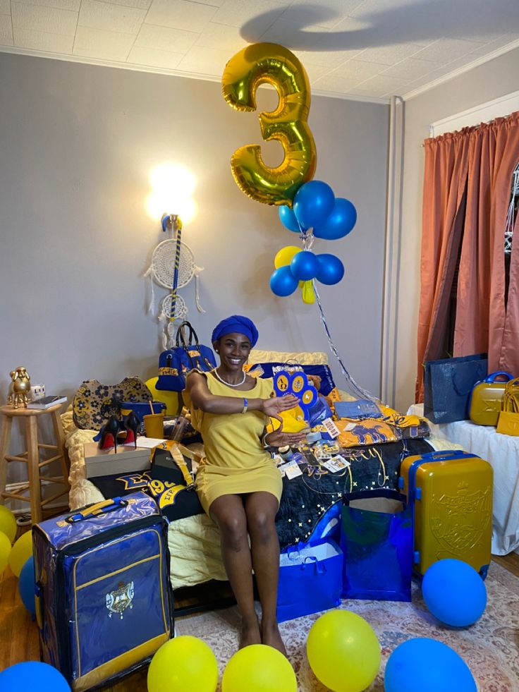 a woman sitting on top of a bed surrounded by blue and yellow balloons in the shape of numbers