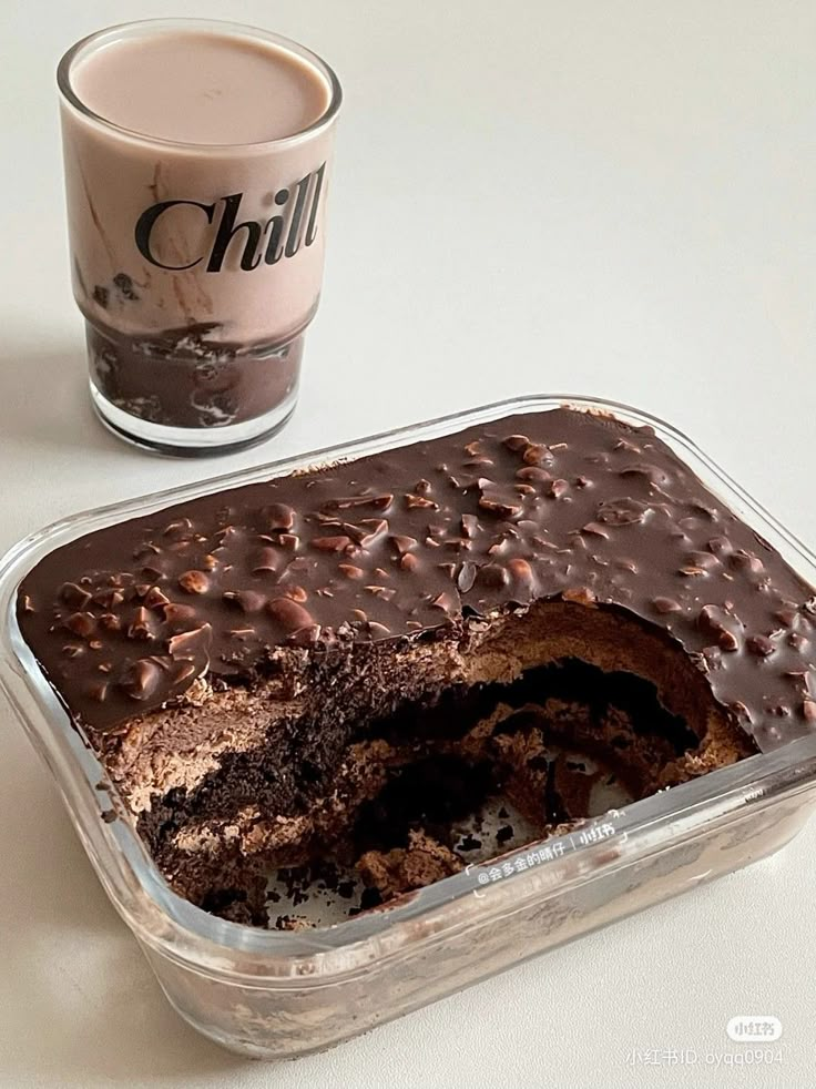 a chocolate cake in a plastic container next to a cup of coffee