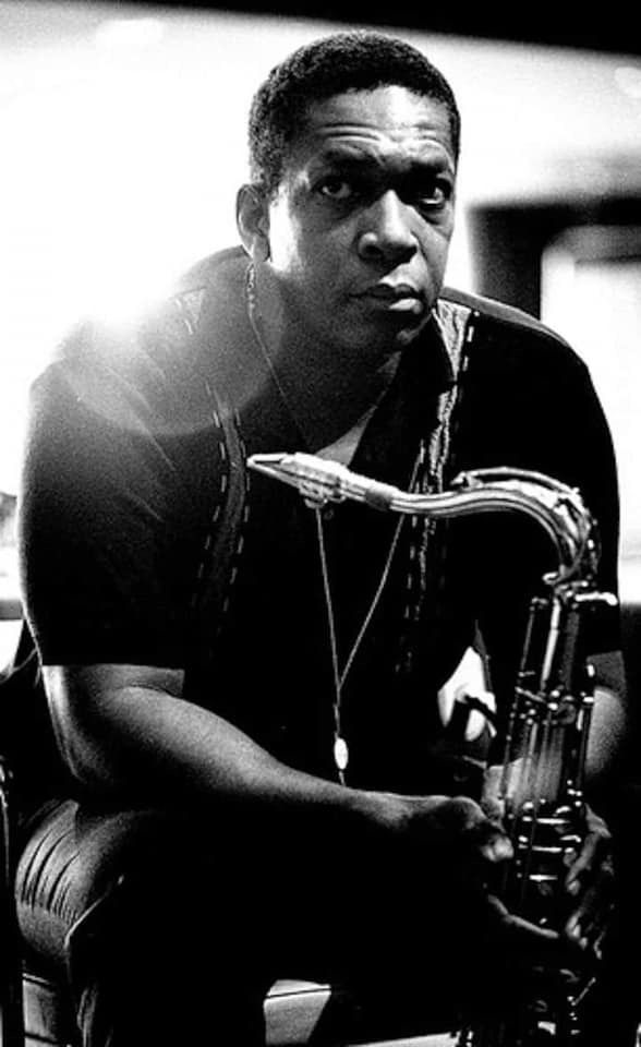 a black and white photo of a man sitting on a chair with a saxophone in his hand