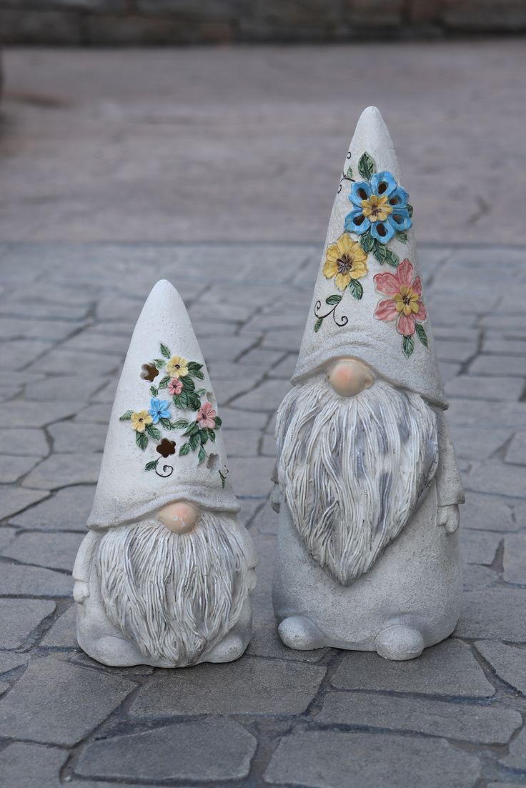 two garden gnomes with flowers on their hats are sitting on the ground next to each other