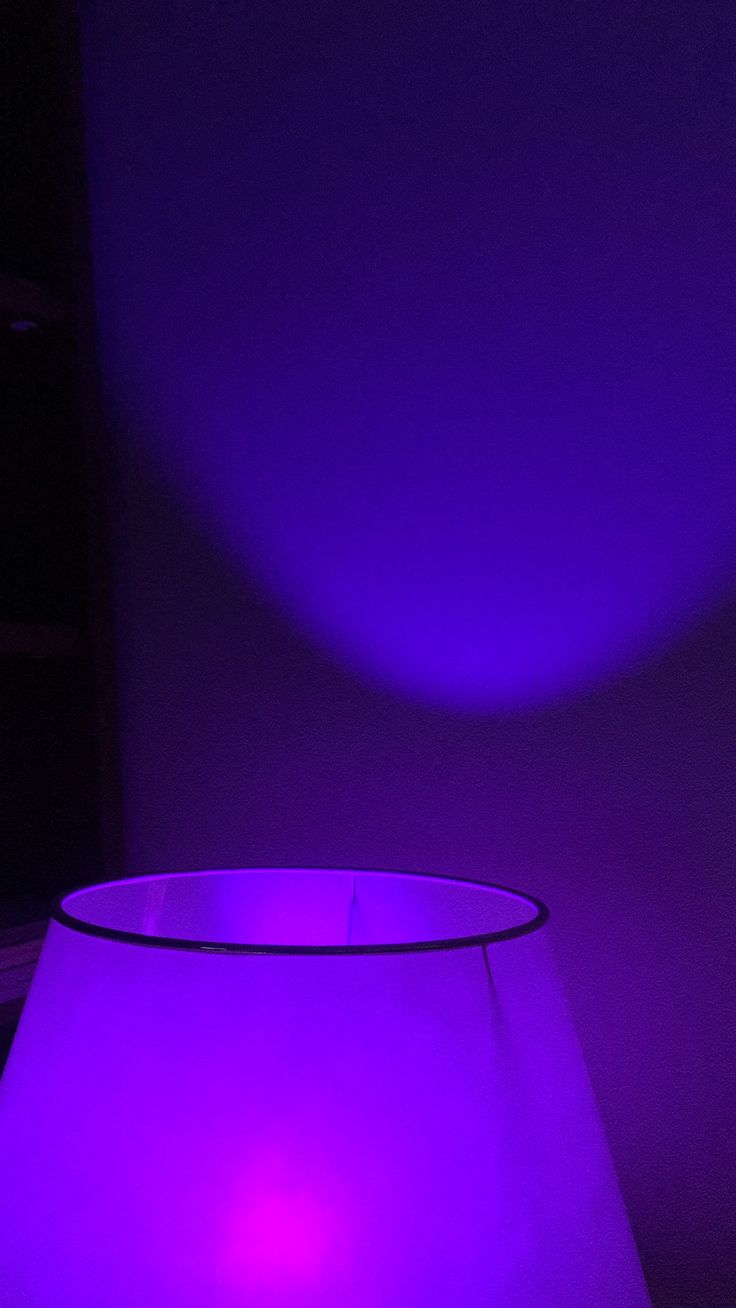 a purple light shines brightly on the surface of a table lamp in a dark room