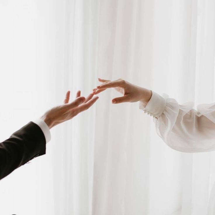 two people reaching out their hands to each other in front of a window with white curtains