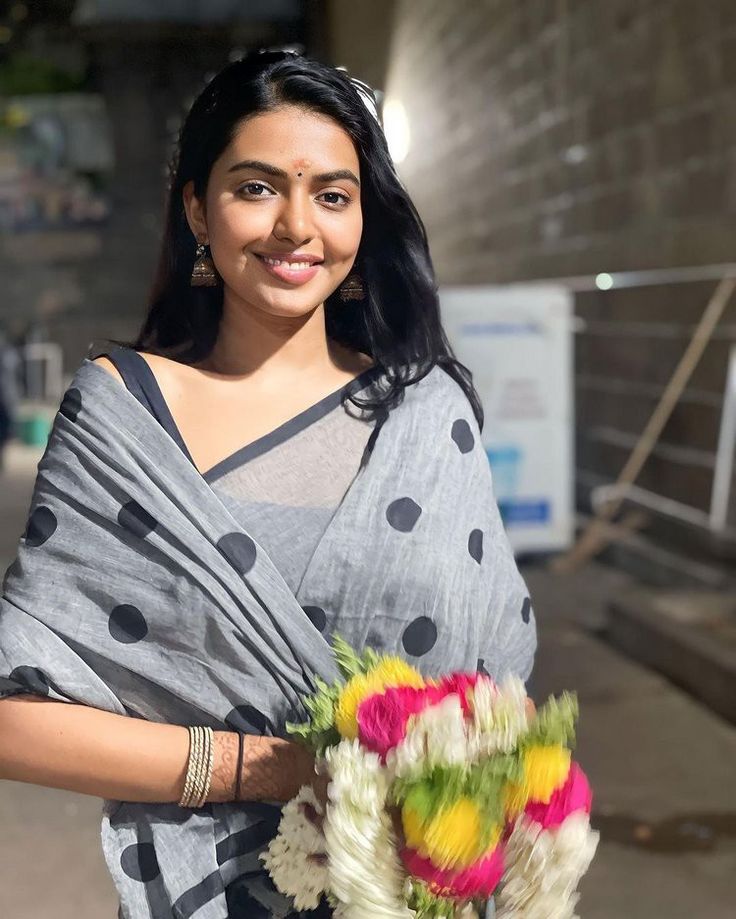 a woman holding a bouquet of flowers in her hand and wearing a sari with dots on it