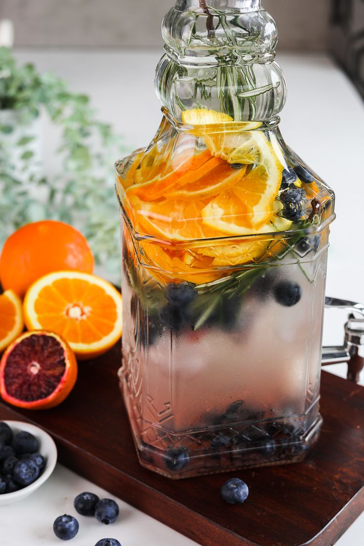 a pitcher filled with liquid next to sliced oranges and blueberries