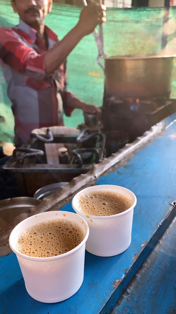 two white cups filled with liquid sitting on top of a blue table next to a man