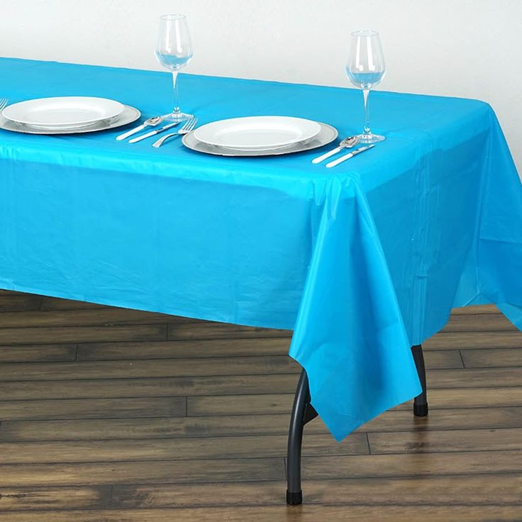 a blue table cloth with white plates and silverware on it is sitting in front of two empty wine glasses