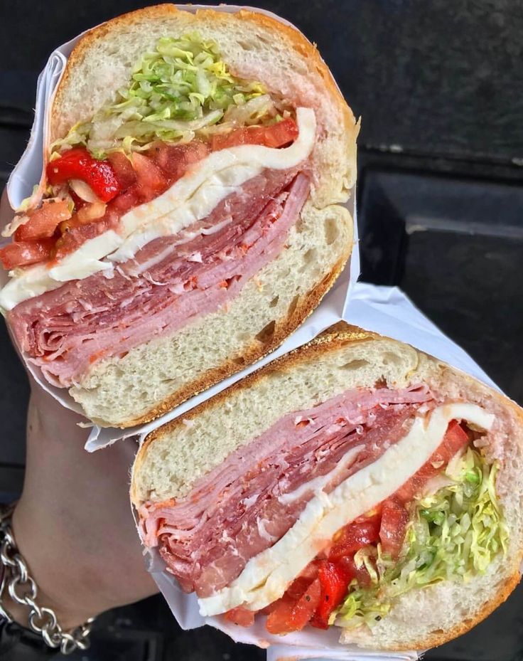 two halves of a sandwich with meat, lettuce and tomato on it being held by someone's hand