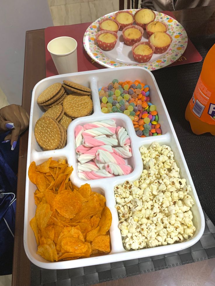 a tray filled with lots of food next to a bottle of orange juice and cupcakes