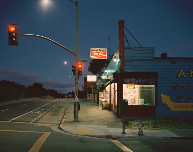 an empty street corner at night with a red traffic light and storefronts in the background