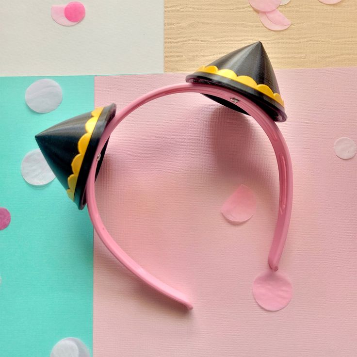 a pink headband with two black and yellow hats on it, sitting on a multi - colored background