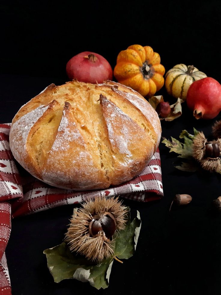 a loaf of bread sitting on top of a red and white checkered cloth next to some fruit