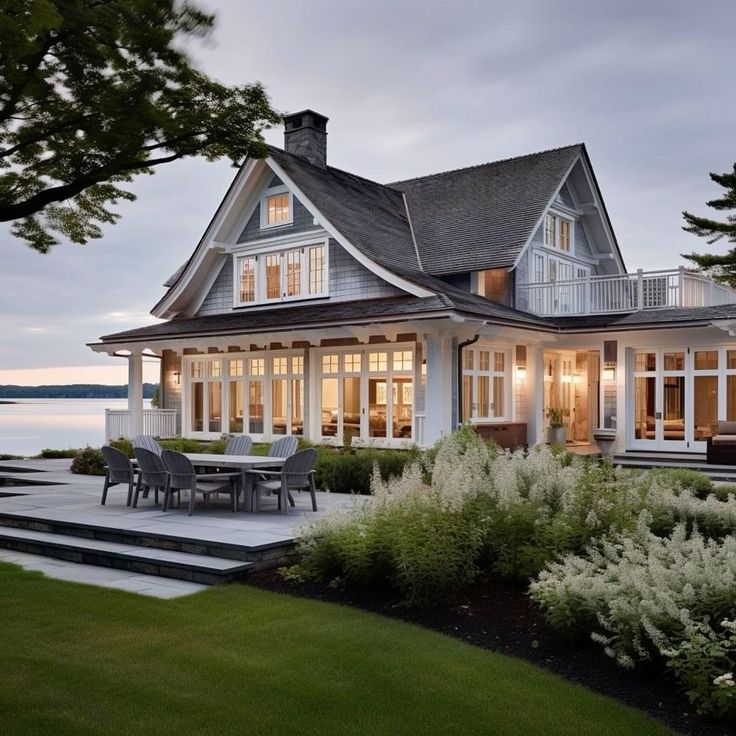 a house that is next to the water with lots of windows and plants in front of it