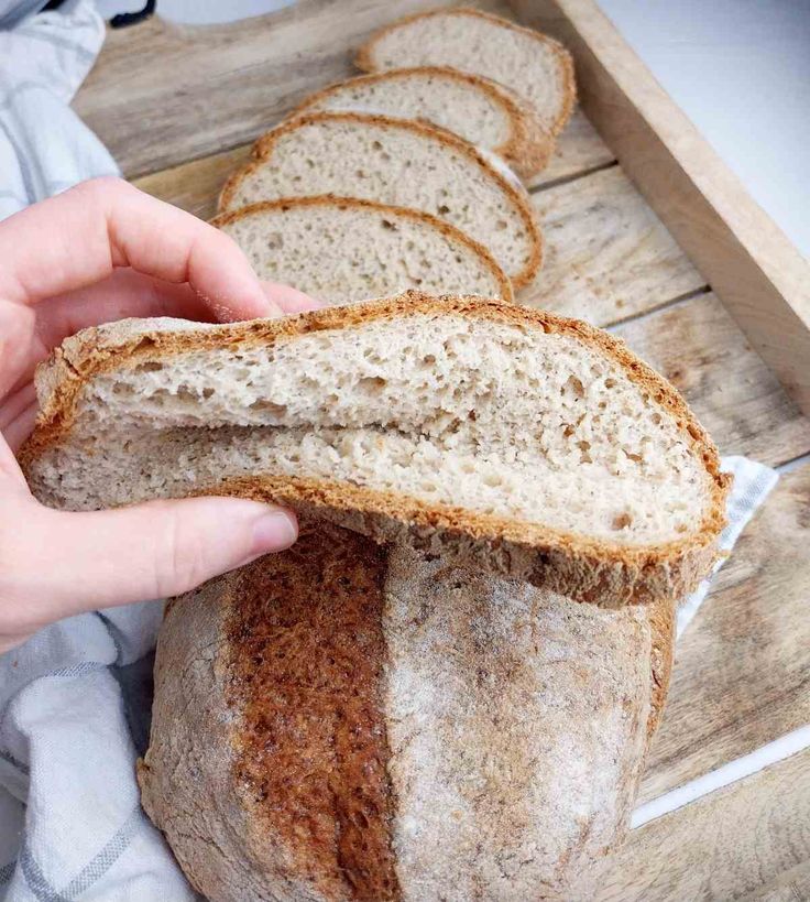 a person holding a loaf of bread in front of it on a cutting board with slices cut out