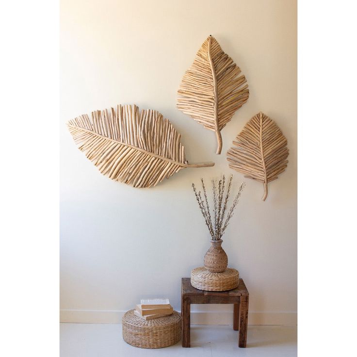 three woven leaves hang on the wall next to a small table with a vase and plant