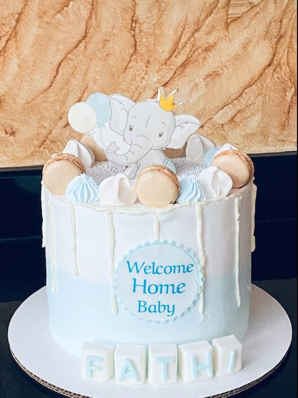 a baby shower cake with an elephant on top and welcome home baby written in blue