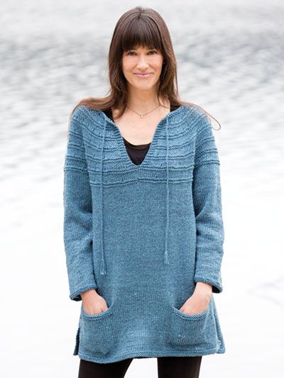 a woman standing on the beach wearing a blue sweater and black leggings with her hands in her pockets