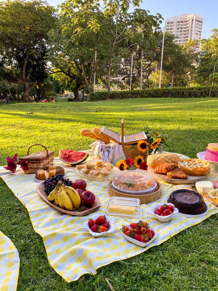 a picnic with fruit, cake and bread on a blanket in the middle of a park