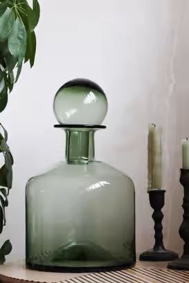 a green glass bottle sitting on top of a table next to two candles and a potted plant