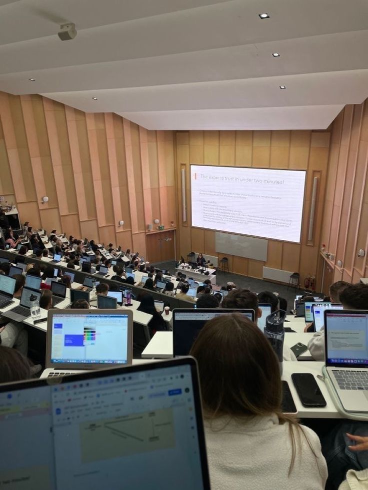 people sitting at tables with laptops in front of them and a projector screen behind them