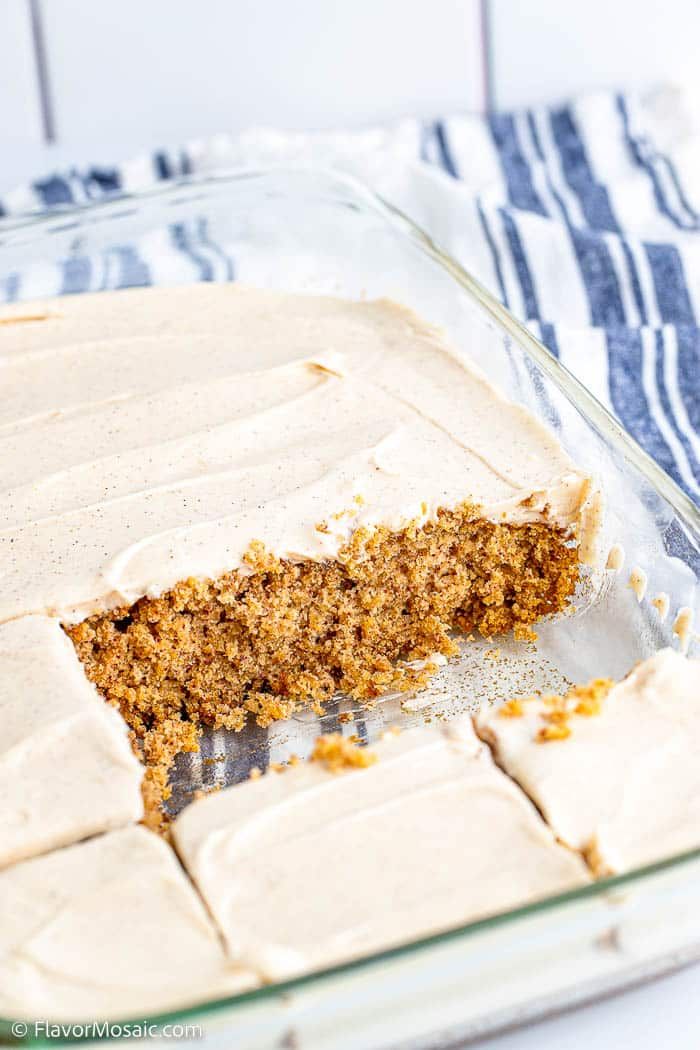 carrot cake with cream cheese frosting in a glass pan on a blue and white towel