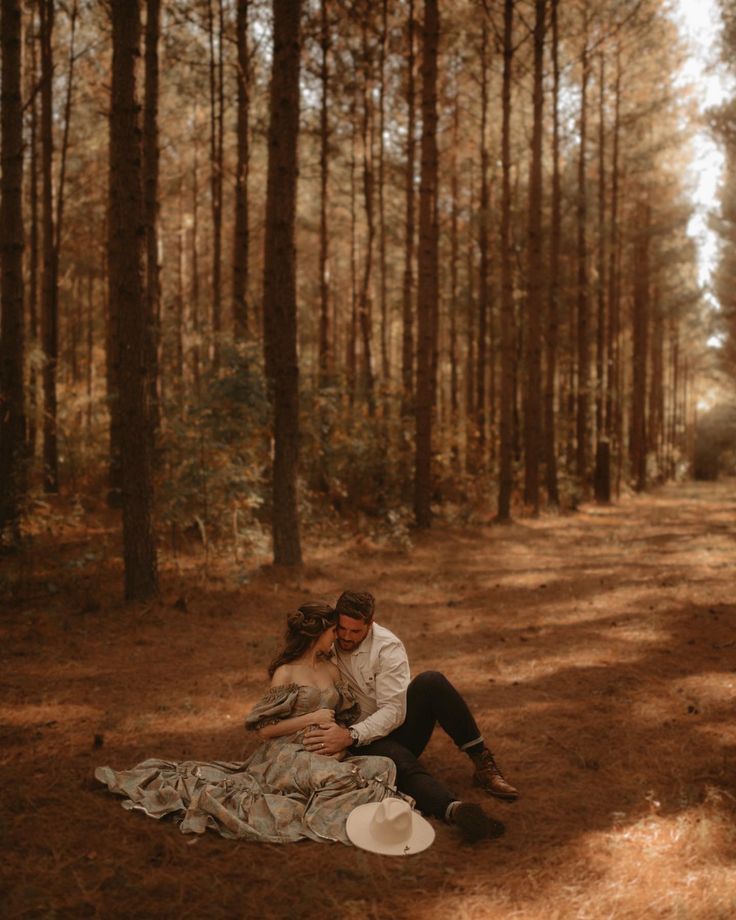 a man and woman sitting on a blanket in the woods