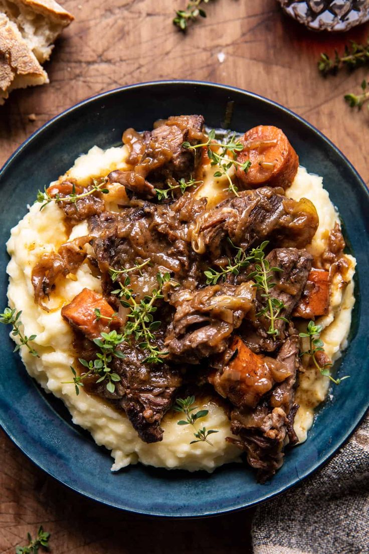 a blue plate topped with mashed potatoes covered in beef and gravy on top of a wooden table