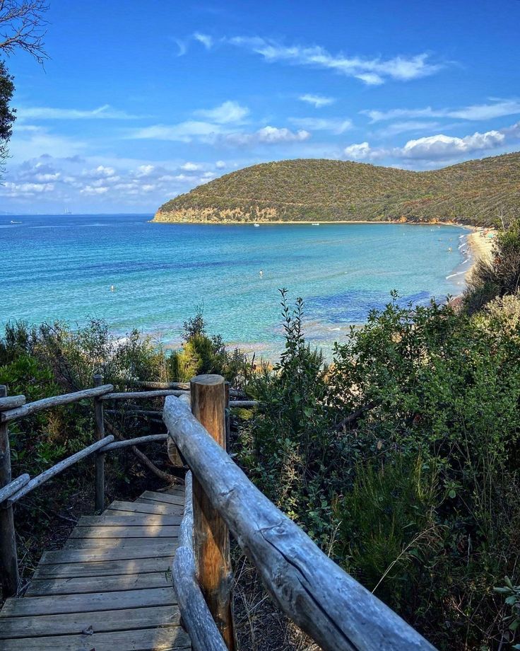 a wooden walkway leading to the beach with blue water and hills in the back ground