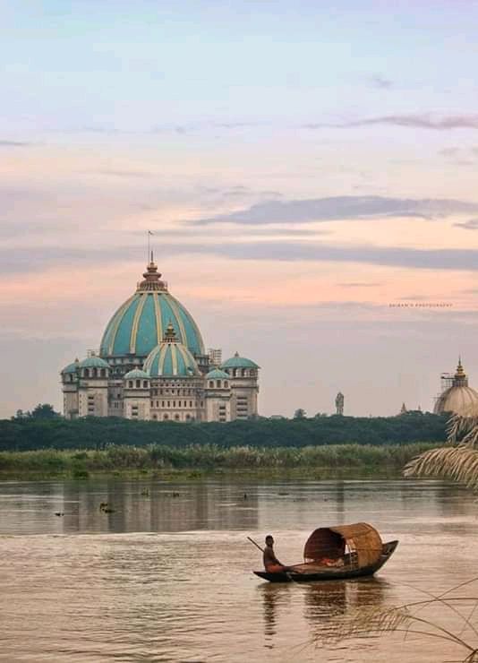 two people on a small boat in the water near a large building with a dome