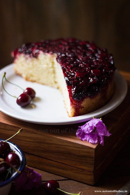 a piece of cake sitting on top of a white plate next to a bowl of cherries