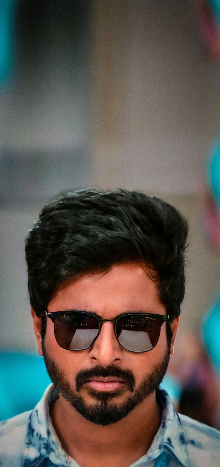 a man with dark hair and sunglasses looking at the camera