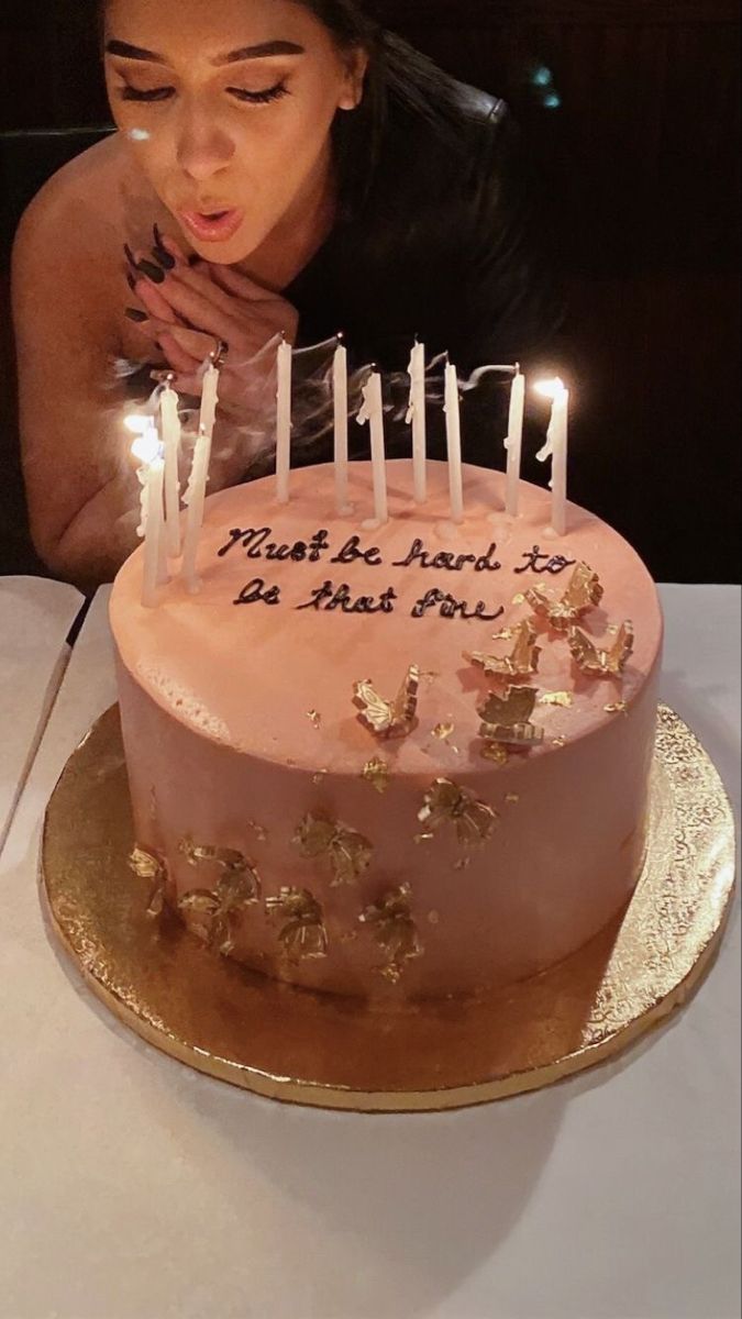 a woman blowing out candles on a cake with pink frosting and gold foil decorations