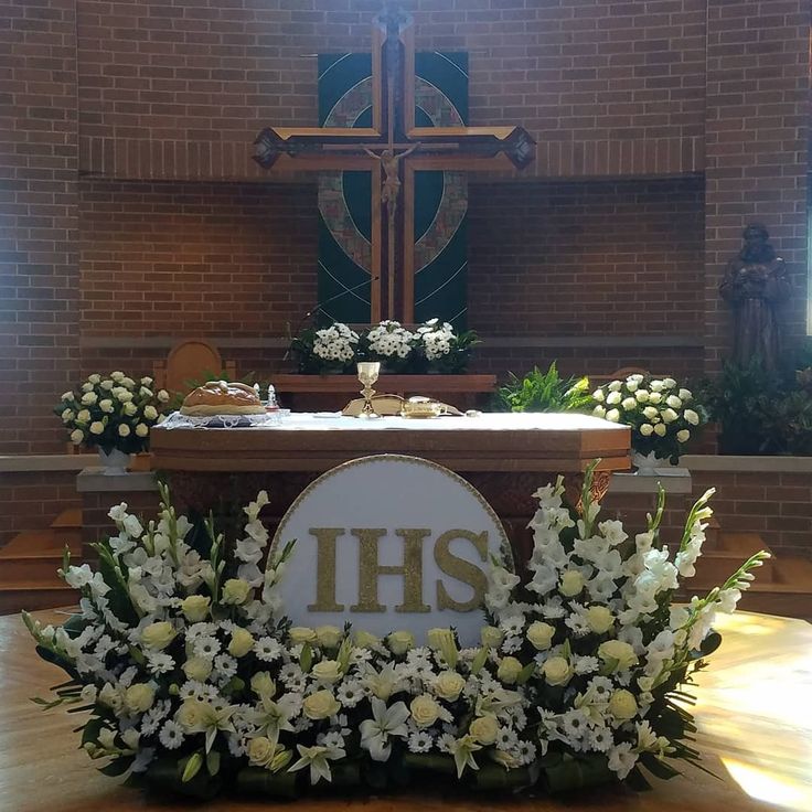 flowers and greenery decorate the front of a church alter with an ihs sign