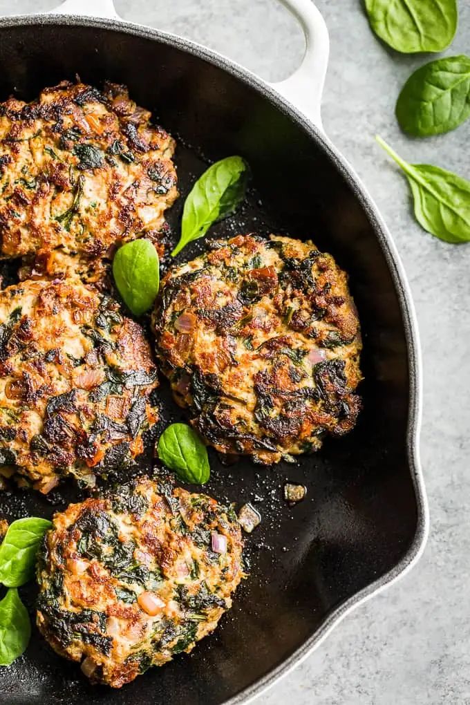 four patties in a skillet with spinach leaves on the side