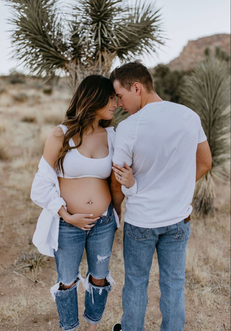 a pregnant couple standing next to each other in front of a joshua tree and cactus