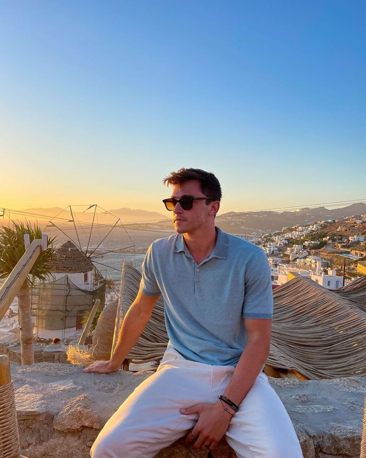 a man sitting on top of a stone wall next to the ocean with buildings in the background