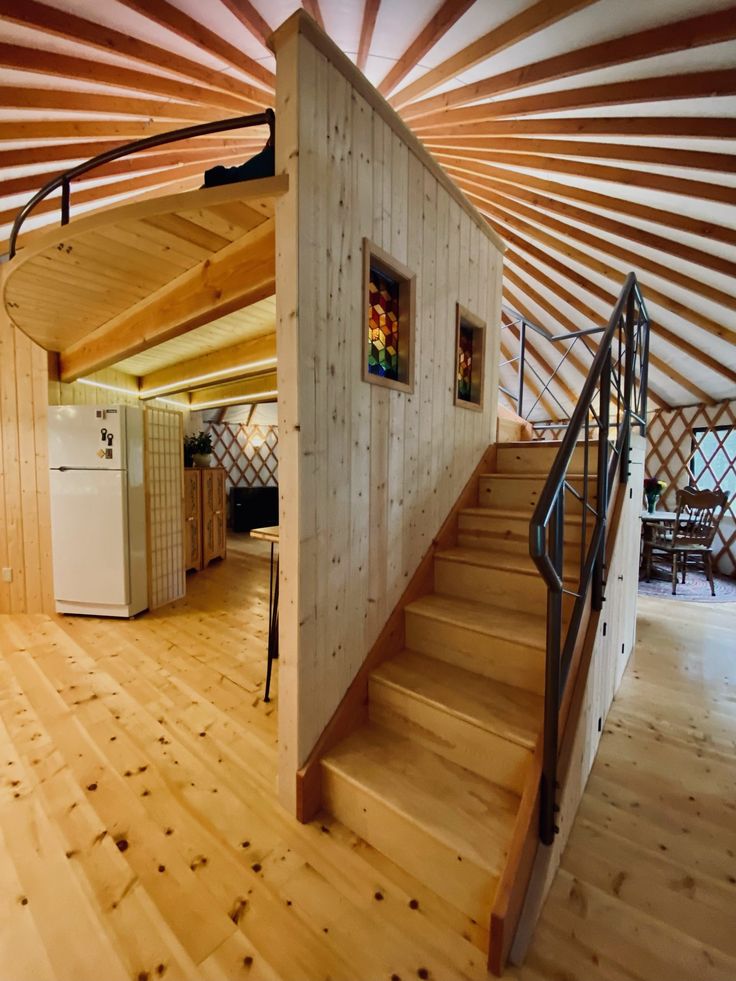 the interior of a yurt with wooden floors and stairs leading up to an open kitchen area