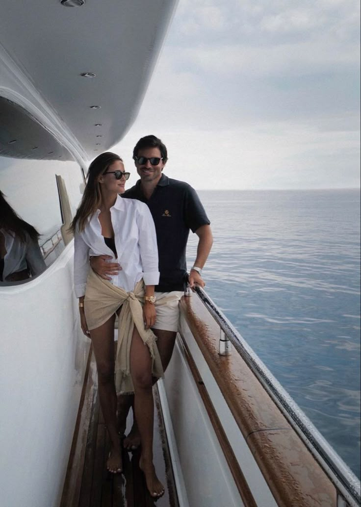 a man and woman standing on the side of a boat looking out at the ocean