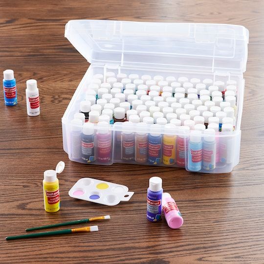 an open plastic box filled with lots of different colored paints and paintbrushes on a wooden table