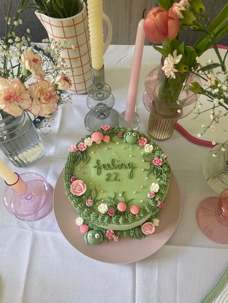 a green cake sitting on top of a table next to vases filled with flowers