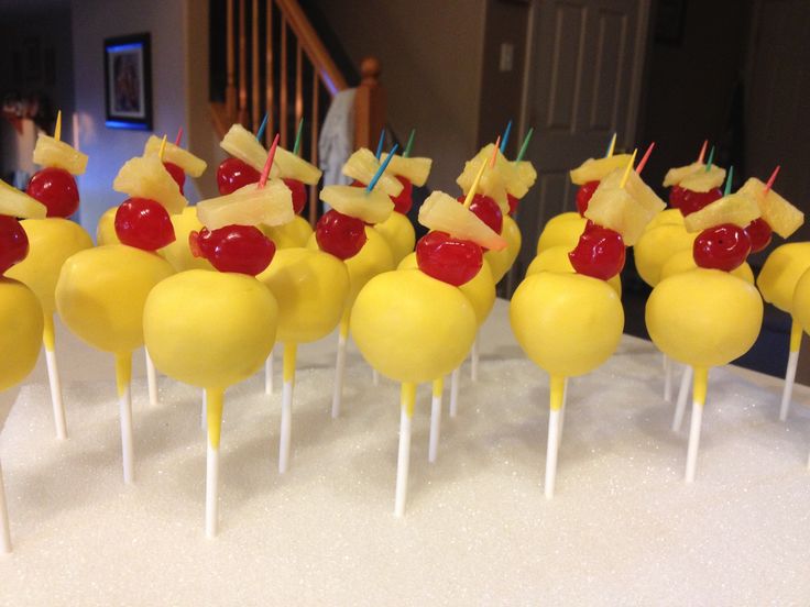 there are many yellow cake pops with cherries and pineapples on them in the shape of animals