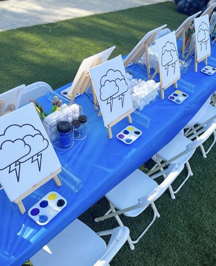 a blue table topped with lots of easels and paintings on top of green grass