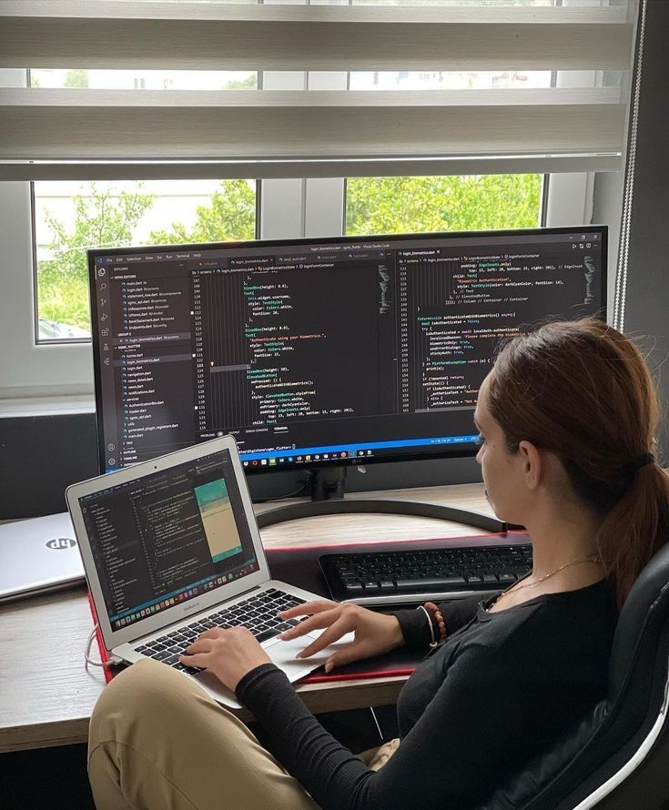 a woman is sitting in front of two computer screens and typing on her laptop keyboard